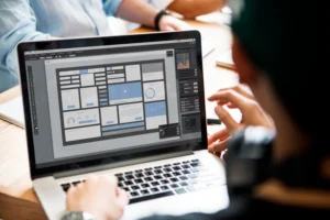 Person designing a UI layout on a laptop screen in a bright workspace.